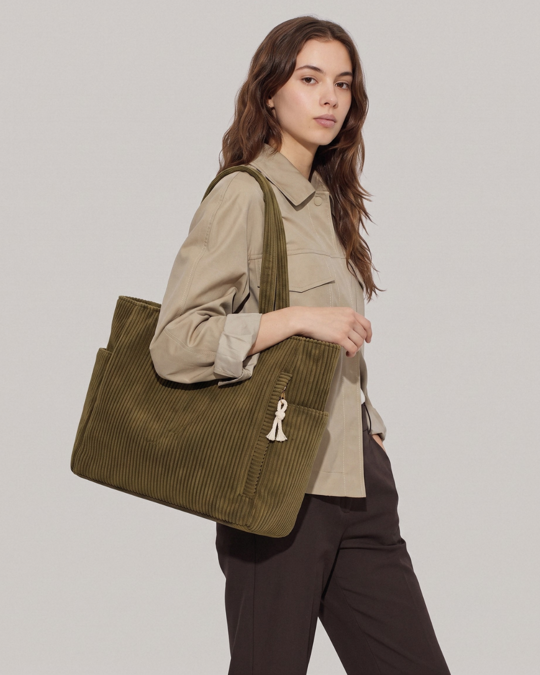 Khaki sztruksowa torebka Cordi noszona na ramieniu przez modelkę w stylizacji z koszulą, podkreślająca jej dopasowanie do jesienno-zimowych zestawów.