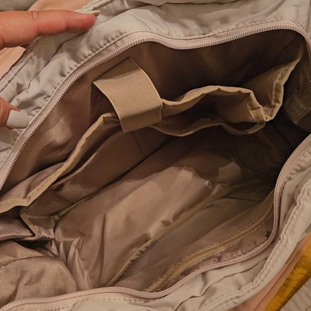 „Beżowa torba otwarta z góry, widoczne wnętrze z przegrodami, kieszenią na zamek i elastycznym paskiem; praktyczny organizer.”