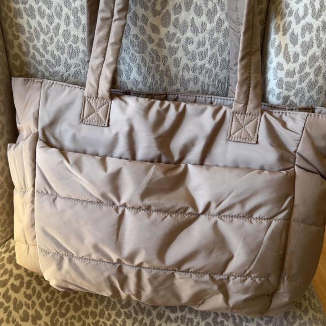 „Beżowa pikowana torba położona na fotelu z tkaniną w panterkowy wzór; miękka faktura materiału i elegancki wygląd.”