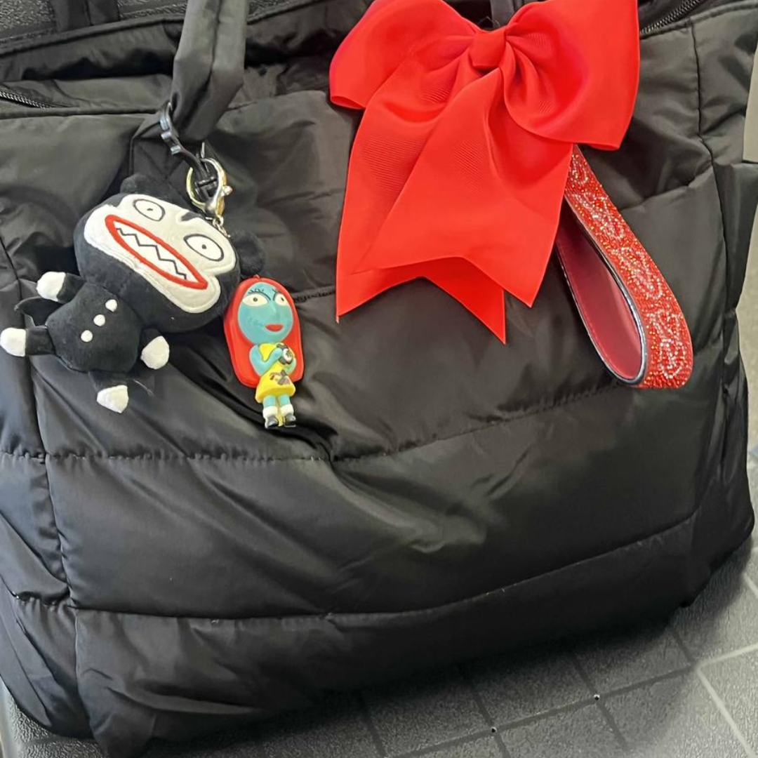 „Czarna pikowana torba z dużą czerwoną kokardą i kolorowymi brelokami przedstawiającymi postacie; detal ozdobny w stylu playful.”