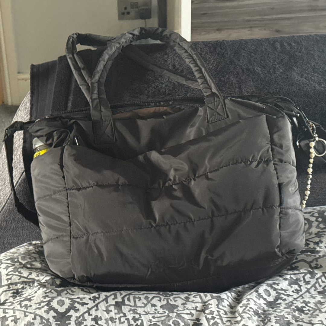 „Czarna pikowana torba leżąca na sofie, z ozdobnym brelokiem z pereł i widocznym bokiem; elegancki, codzienny styl.”