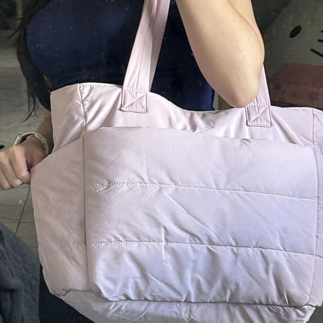 „Różowa pikowana torba na ramię trzymana przez osobę w granatowej bluzce; zdjęcie wykonane przed lustrem.”