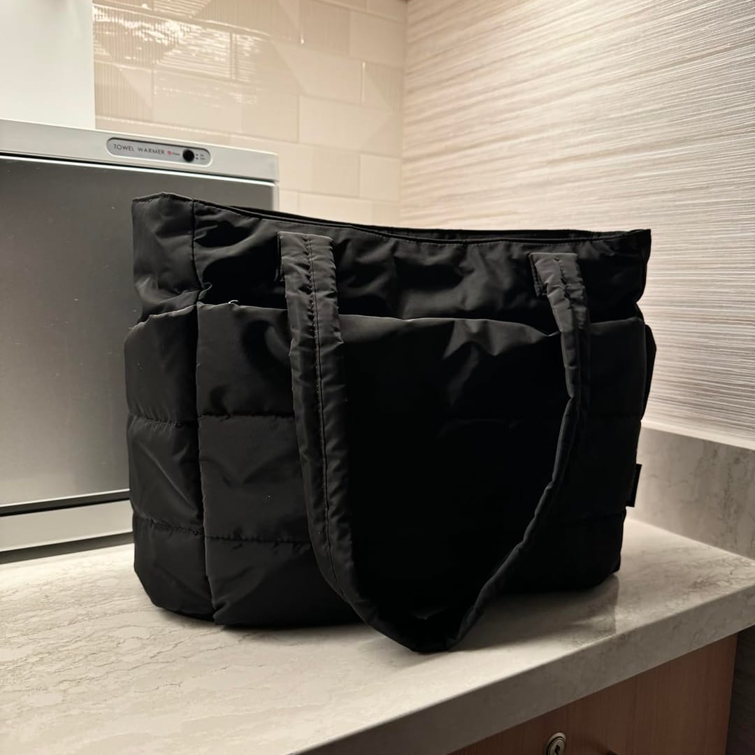 „Czarna torba Softi ustawiona na blacie w łazience; widoczne pikowane boki i długie uszy torby.”