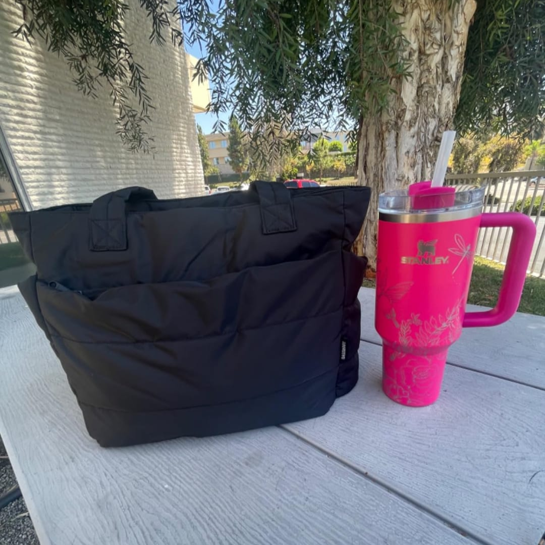„Czarna torba Softi na zewnątrz, ustawiona na ławce piknikowej; obok duży różowy kubek termiczny ze słomką, w tle drzewo.”
