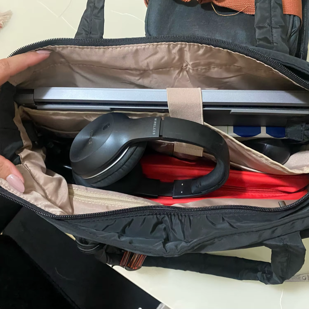 „Czarna torba Softi otwarta z góry, w środku laptop w przegrodzie, słuchawki nauszne i czerwona saszetka; widoczne kieszenie organizera.”