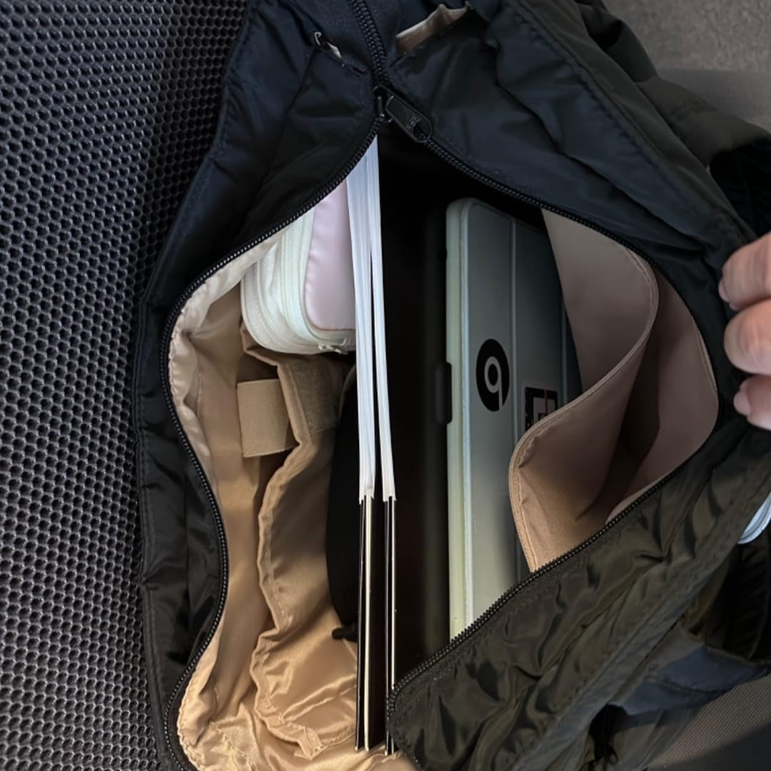 „Czarna torba Softi otwarta z góry; w środku tablet w przegrodzie, notesy i etui, widoczne kieszenie organizera; dłoń trzyma suwak.”