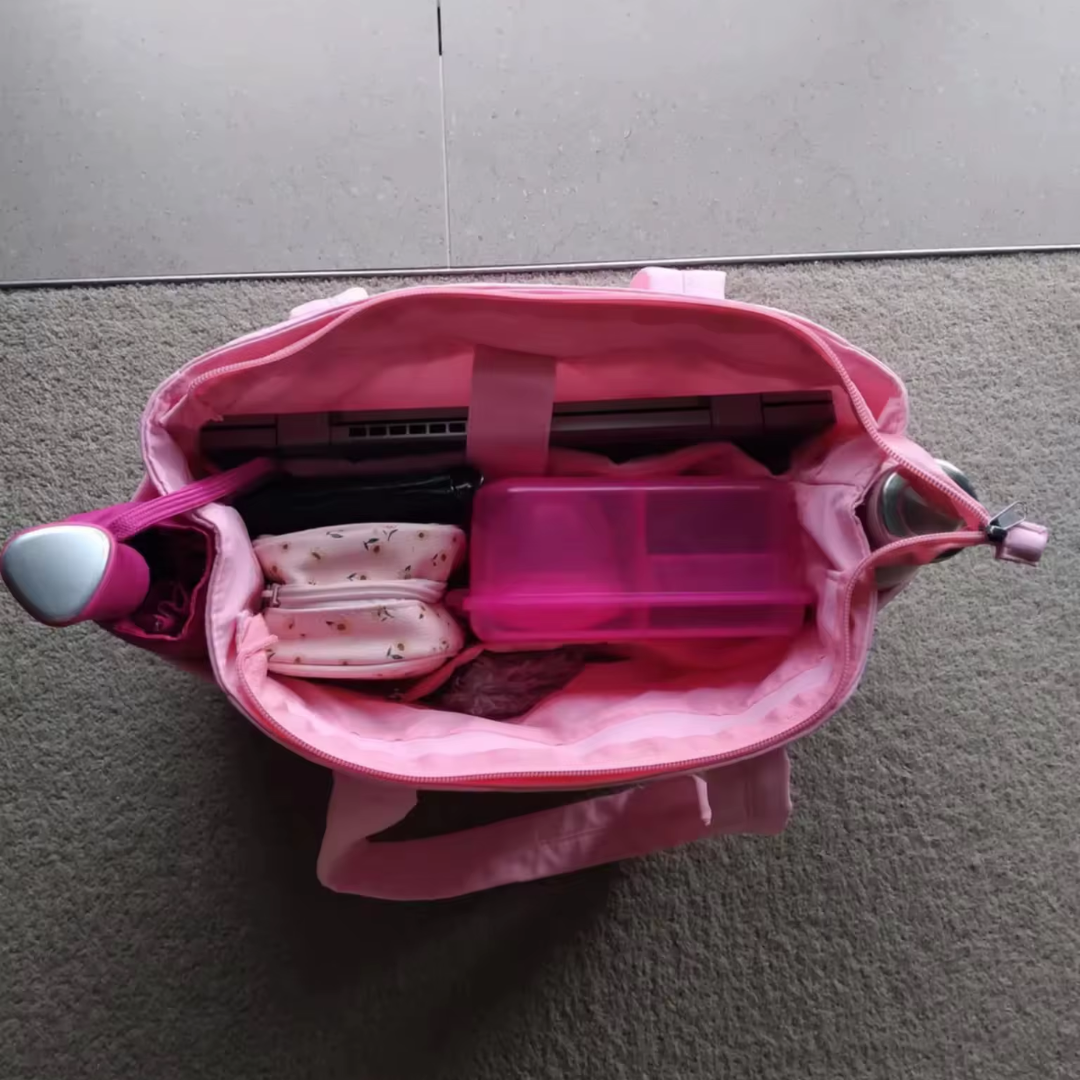 „Różowa torba Softi otwarta z góry; w środku laptop w przegrodzie, różowy organizer, kosmetyczki i butelki po bokach.”