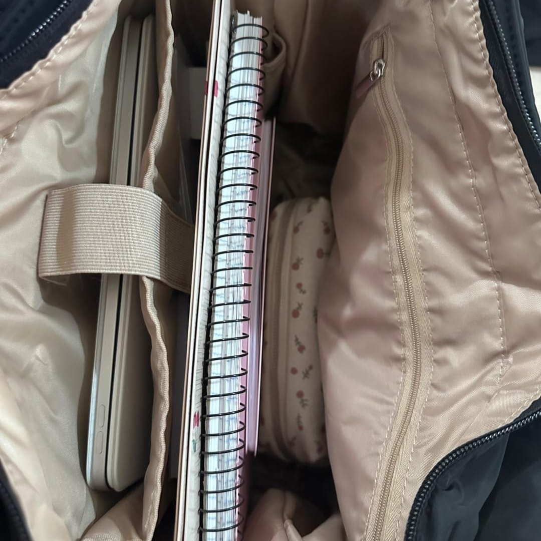 „Zbliżenie wnętrza torby Softi: laptop przypięty paskiem w przegrodzie, obok spiralne notesy i kosmetyczka, po prawej kieszeń na zamek.”